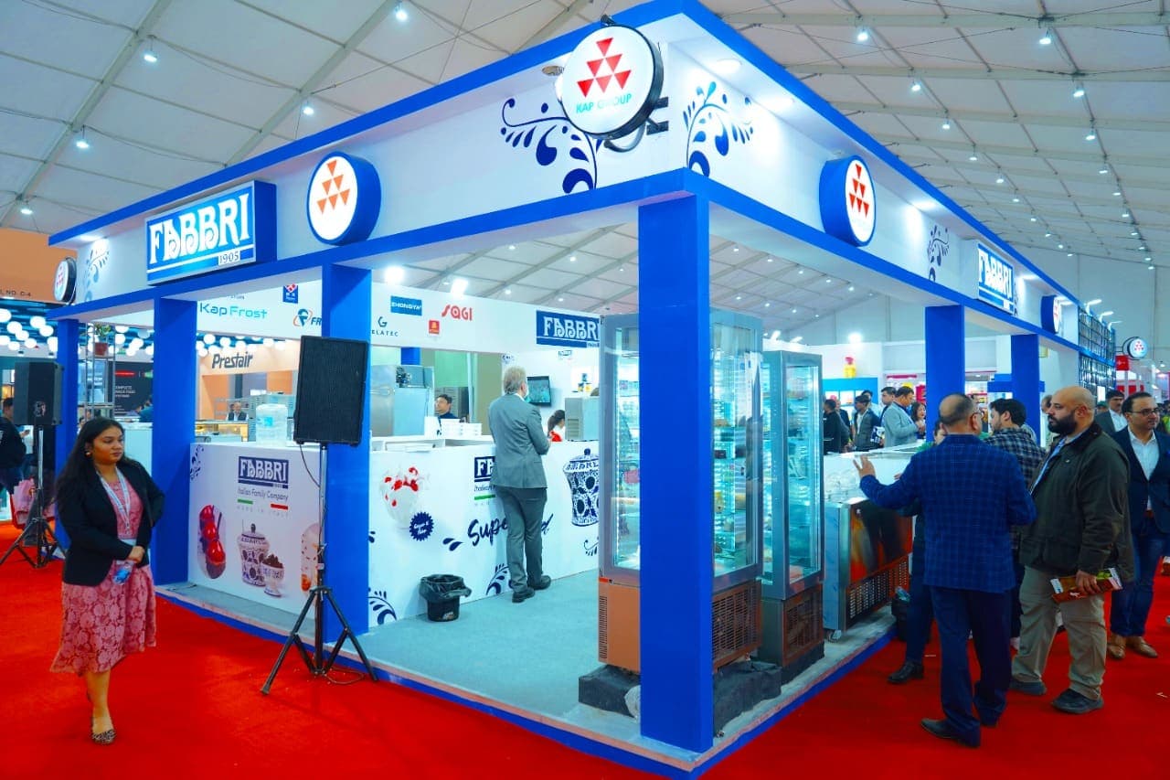 Visitors walk past a brightly lit exhibitor stall